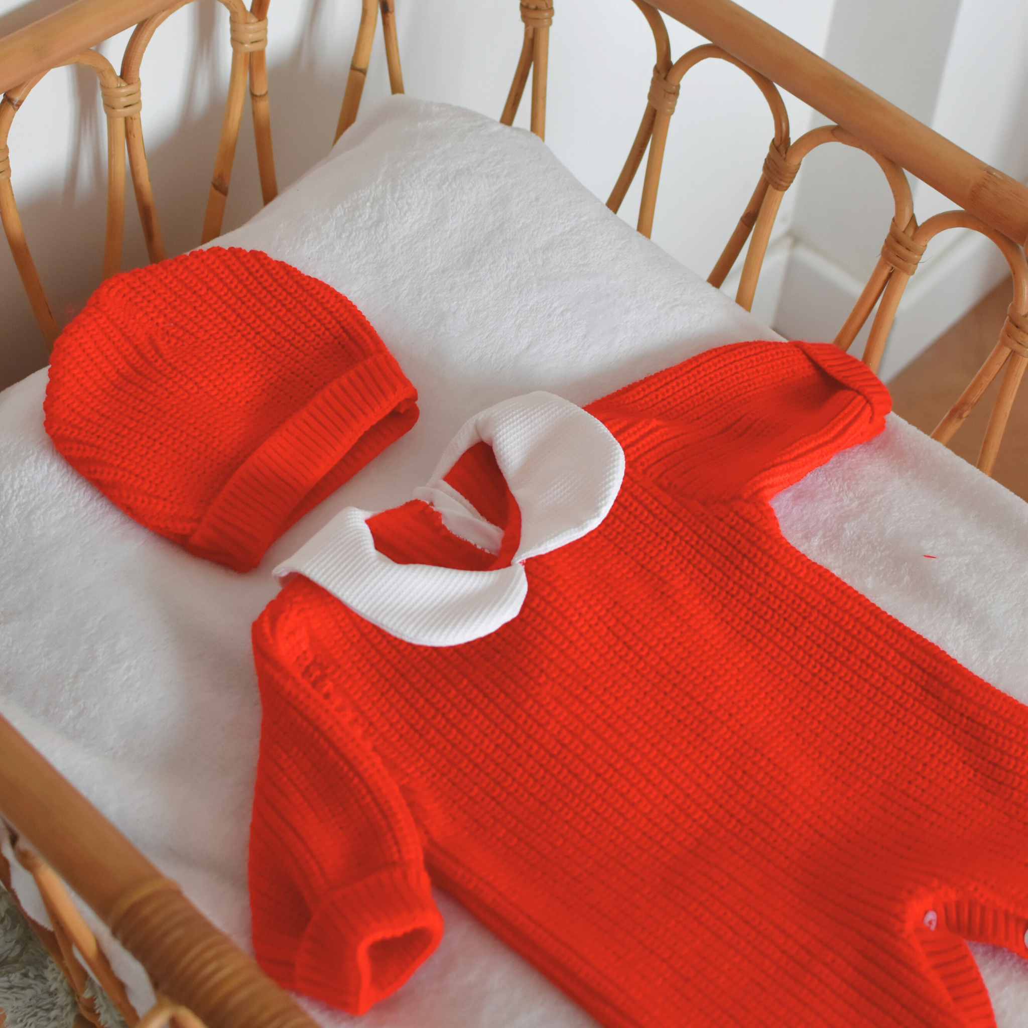 Ensemble naissance rouge en tricot coton avec bonnet dans un berceau