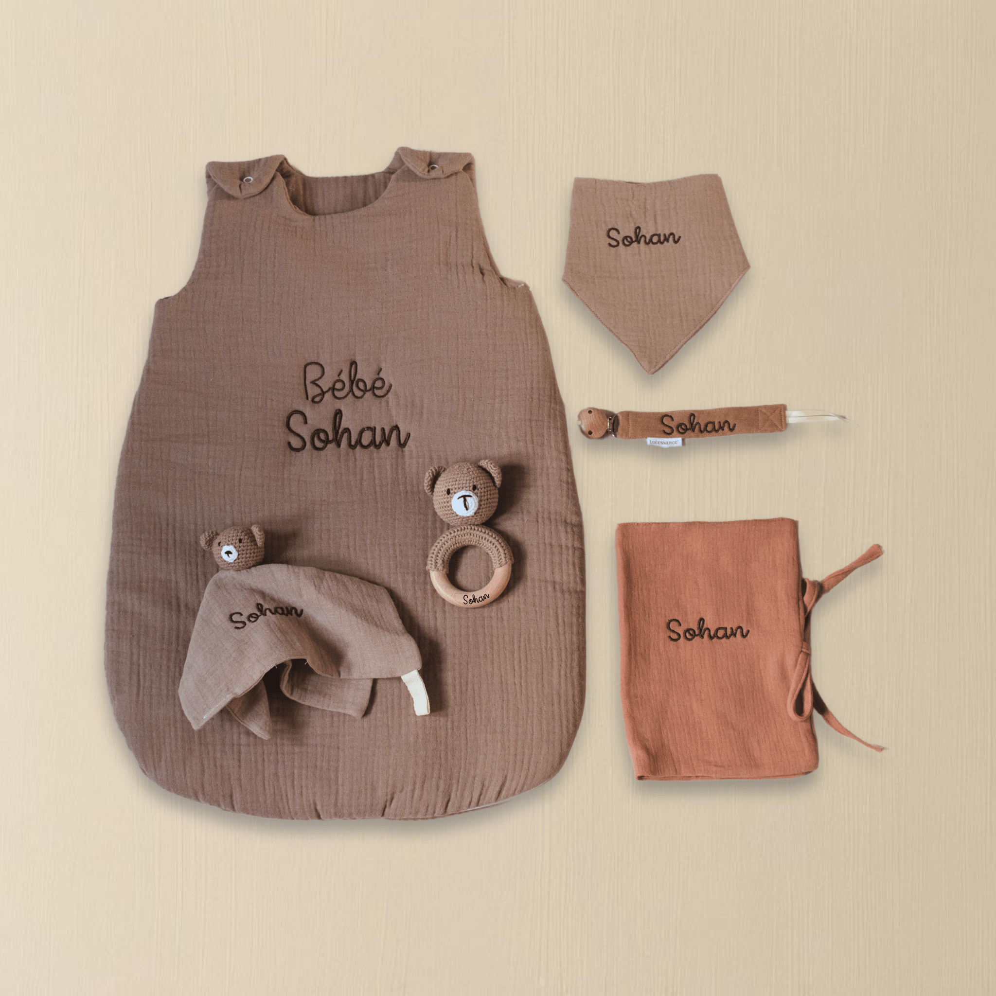 Coffret naissance personnalisé marron avec gigoteuse, bavoir, doudou, hochet et protège-carnet brodés au prénom Sohan, présentation à plat sur fond beige.