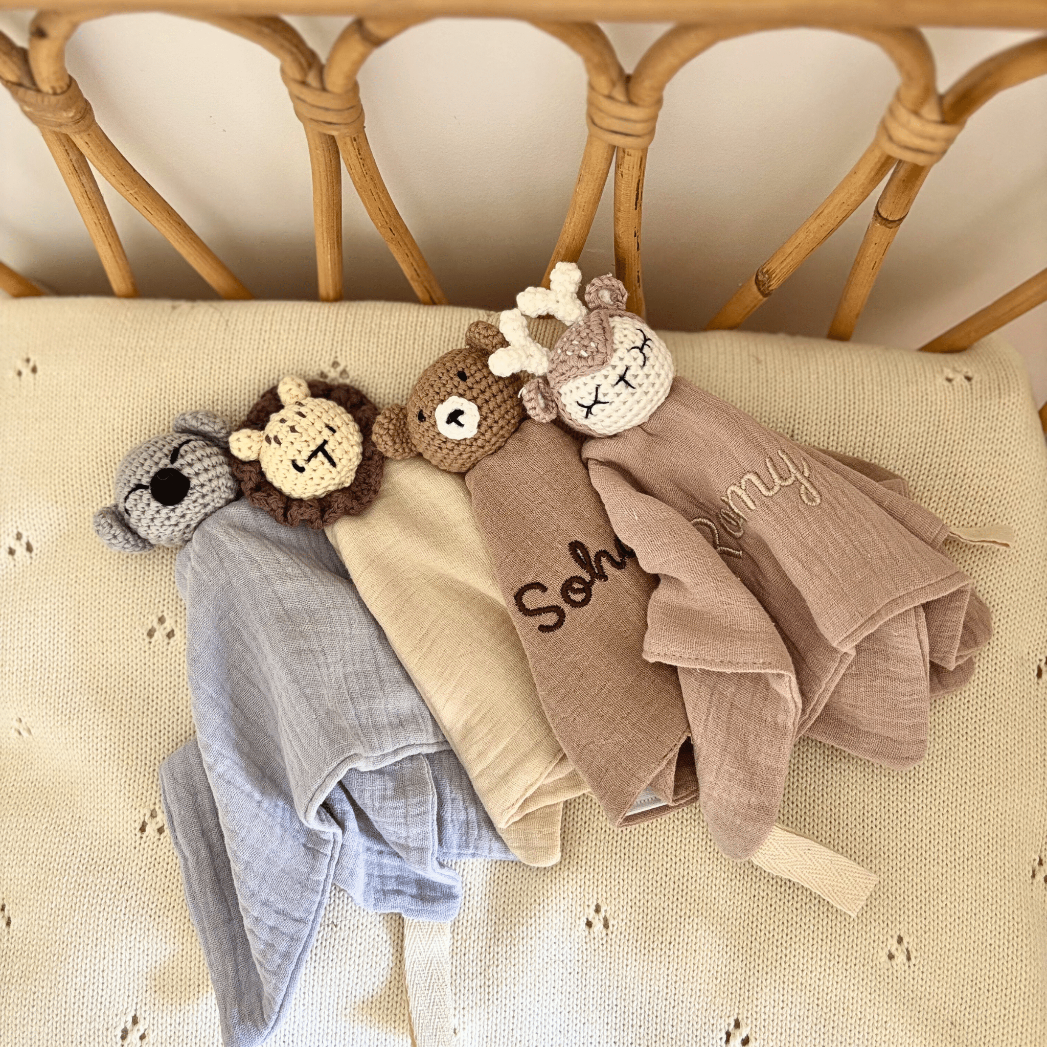 Quatre doudous plats en coton gaufré personnalisés, représentant un koala, un lion, un ours et une biche, brodés aux prénoms Sohan et Romy, posés sur un plaid beige.